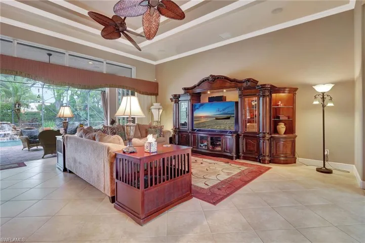 Living area featuring light tile patterned floors, a tray ceiling, a ceiling fan, and ornamental molding