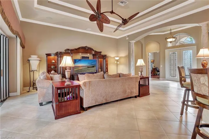 Living room with a tray ceiling, decorative columns, a ceiling fan, visible vents, and arched walkways