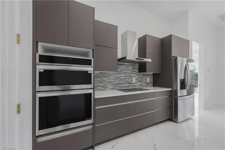 Kitchen featuring modern cabinets, marble finish floor, stainless steel appliances, light countertops, and wall chimney range hood