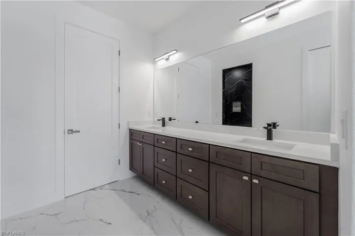 Full bath featuring double vanity, marble finish floor, and a sink