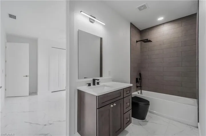 Bathroom with marble finish floor, shower / tub combination, visible vents, and vanity