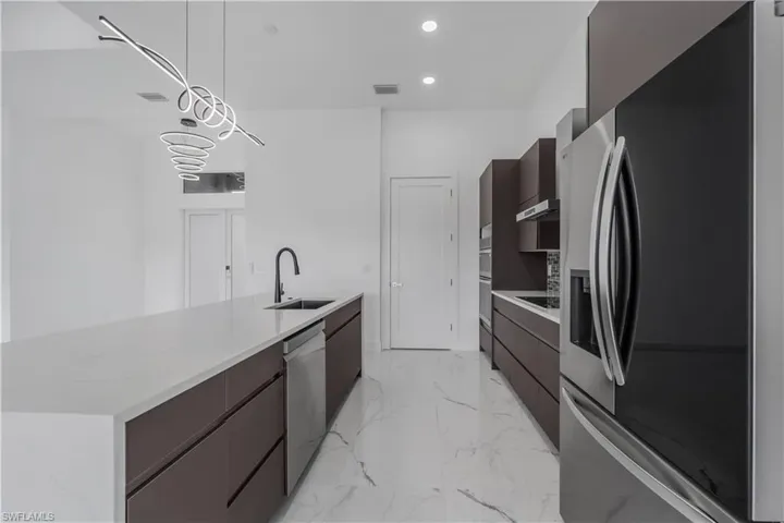 Kitchen with modern cabinets, appliances with stainless steel finishes, hanging light fixtures, light countertops, and a sink