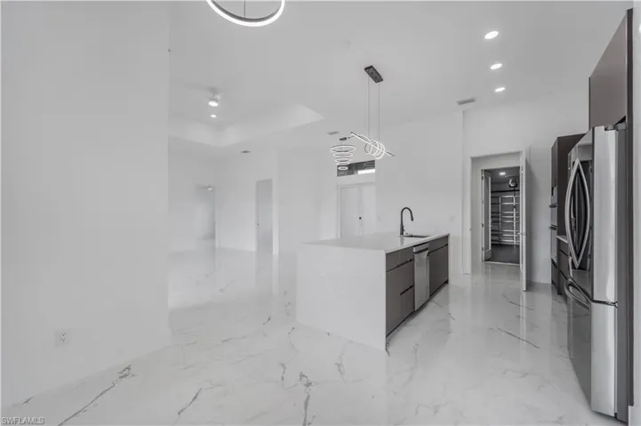 Kitchen featuring stainless steel appliances, a sink, light countertops, hanging light fixtures, and modern cabinets