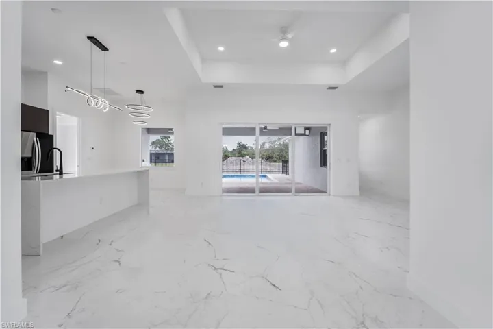 Unfurnished living room featuring marble finish floor, a tray ceiling, a ceiling fan, and recessed lighting