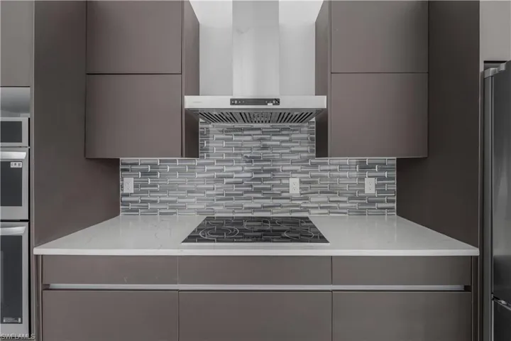Kitchen with stainless steel appliances, range hood, light stone countertops, and modern cabinets