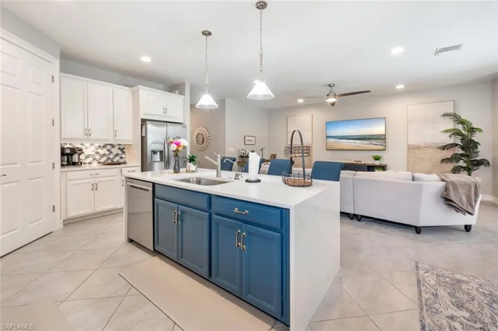 Kitchen with white cabinetry, ceiling fan, stainless steel appliances, and a kitchen island with sink