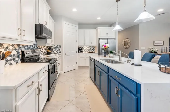 Kitchen featuring tasteful backsplash, stainless steel appliances, white cabinets, sink, and blue cabinetry