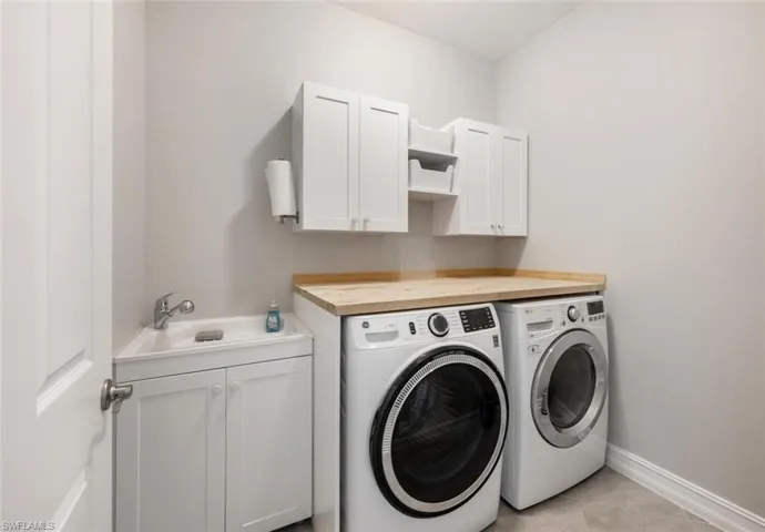 Washroom with cabinets, washing machine and dryer, sink, and light tile patterned floors