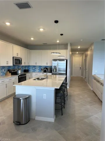 Kitchen featuring range, backsplash, a kitchen island with sink, stainless steel fridge, and sink.