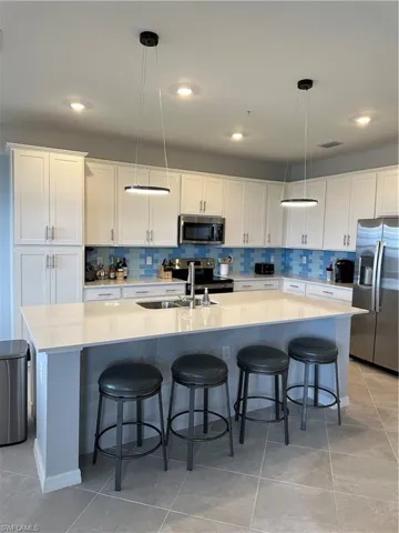 Kitchen featuring decorative light fixtures, white cabinets, refrigerator, and a kitchen island with sink.