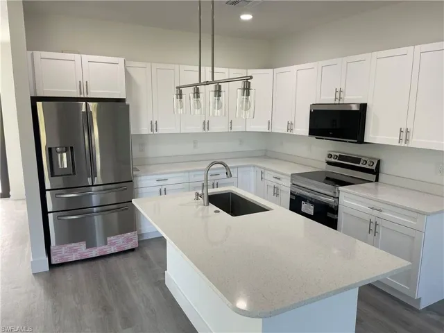 Kitchen featuring sink, white cabinets, stainless steel appliances, and decorative light fixtures