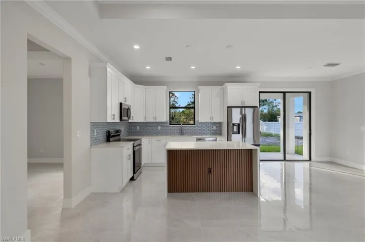 Kitchen with a center island, stainless steel appliances, decorative backsplash, white cabinets, and ornamental molding
