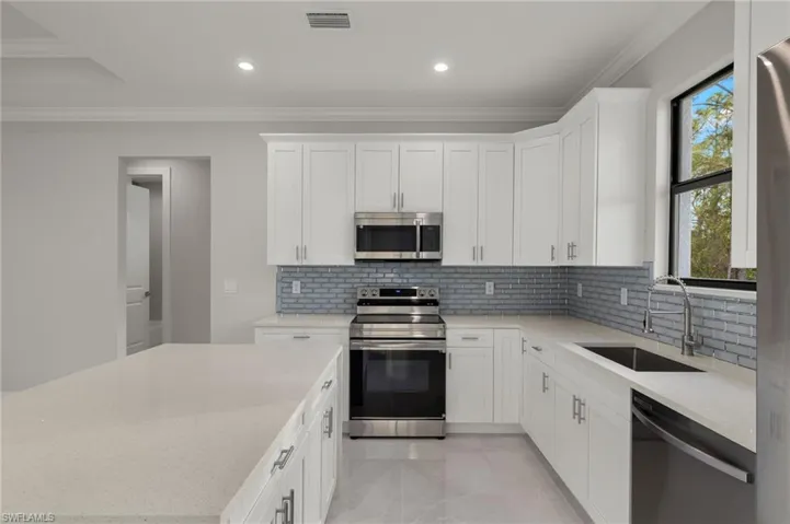 Kitchen with white cabinets, crown molding, sink, and stainless steel appliances