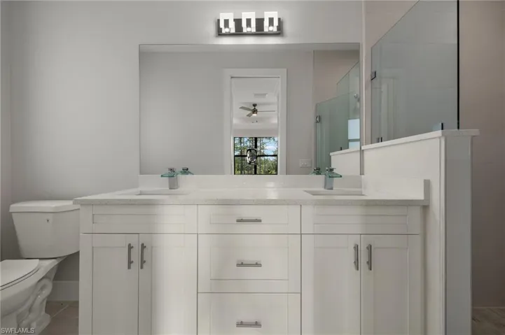 Bathroom featuring an enclosed shower, vanity, toilet, and ceiling fan