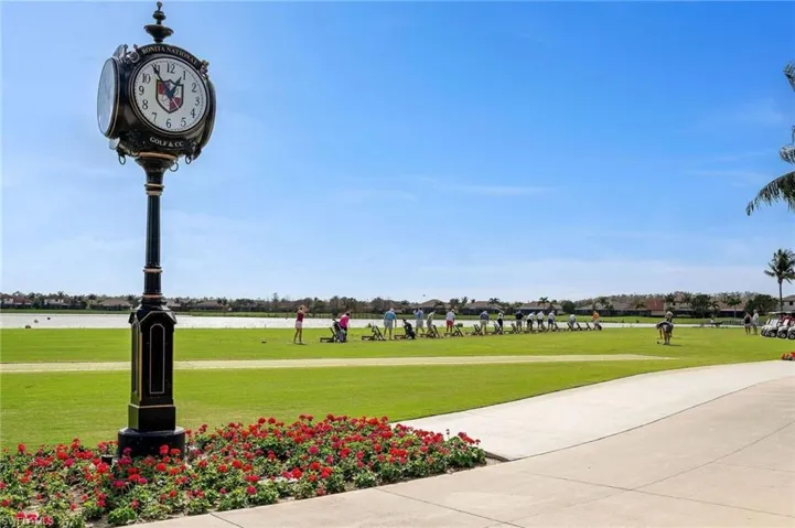 Expansive green space featuring a decorative street clock, a paved pathway, and vibrant red shrubbery