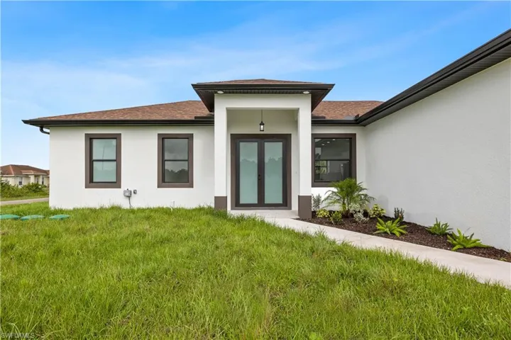 View of exterior entry featuring french doors, stucco siding, a shingled roof, and a lawn