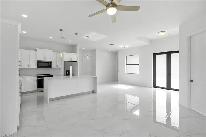 Kitchen with a center island, stainless steel appliances, hanging light fixtures, white cabinets, and a ceiling fan