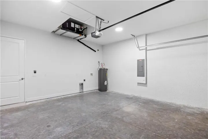 Garage featuring electric water heater, electric panel, recessed lighting, and a garage door opener