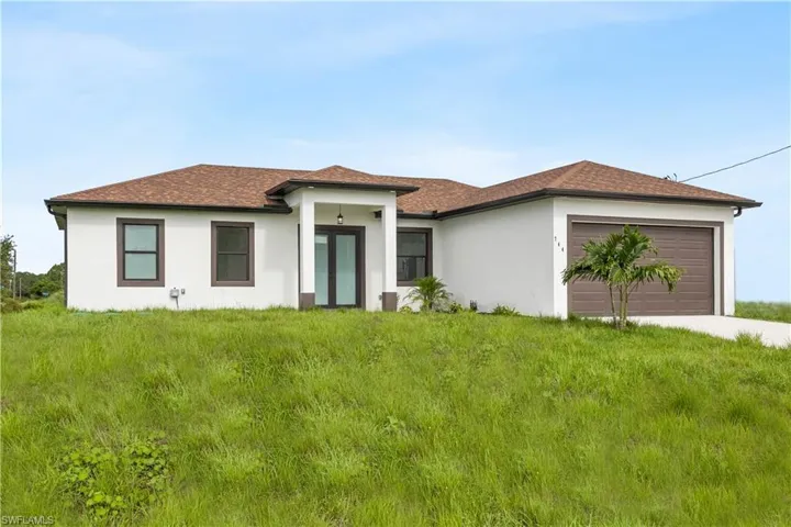 with an attached garage, stucco siding, a shingled roof, a front yard, and concrete driveway