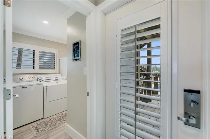 Washroom with ornamental molding, washing machine and clothes dryer, and light wood-style flooring