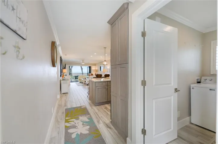 Hall with washer / dryer, wood finish floors, and ornamental molding