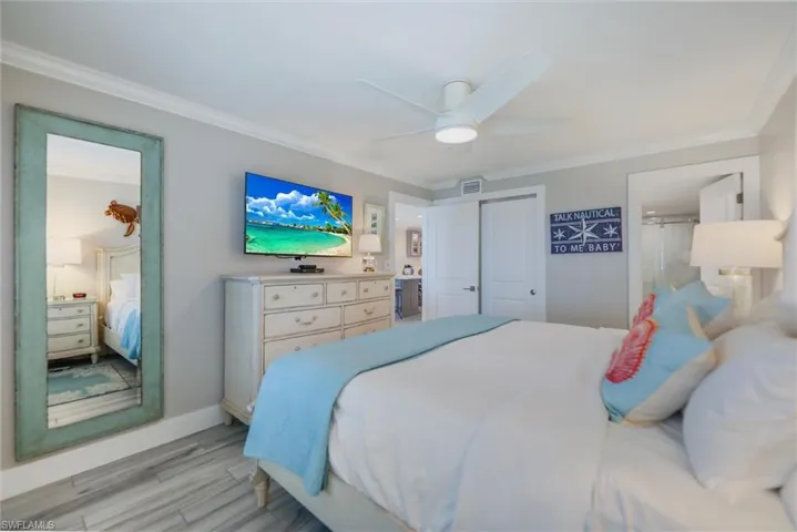Bedroom with ornamental molding, ensuite bathroom, wood finished floors, ceiling fan, and a closet