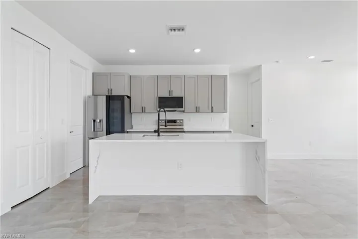 Kitchen with an island with sink, light countertops, gray cabinetry, visible vents, and stainless steel appliances