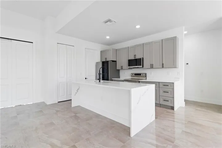 Kitchen featuring stainless steel appliances, visible vents, a center island with sink, and gray cabinets