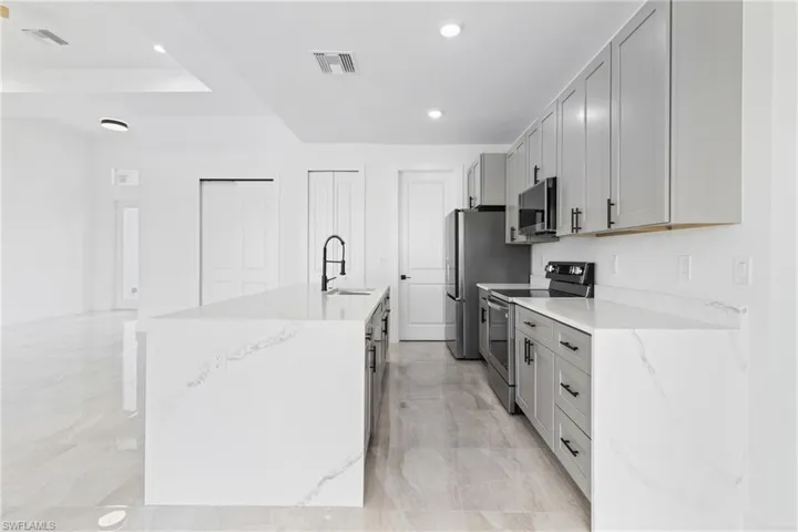 Kitchen with visible vents, a sink, an island with sink, stainless steel appliances, and gray cabinets