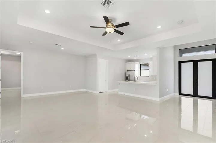 Unfurnished living room with ceiling fan, sink, a tray ceiling, and light tile patterned flooring