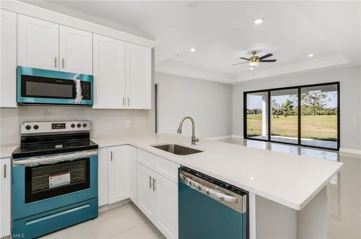 Kitchen with sink, appliances with stainless steel finishes, a tray ceiling, ceiling fan, and kitchen peninsula