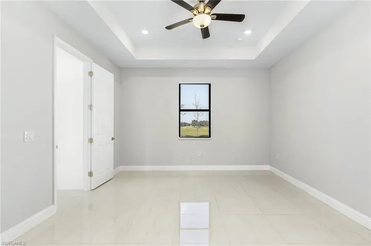 Tiled empty room with ceiling fan and a raised ceiling