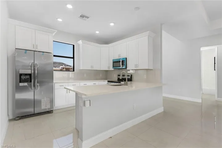 Kitchen featuring tasteful backsplash, white cabinets, appliances with stainless steel finishes, light tile patterned floors, and kitchen peninsula