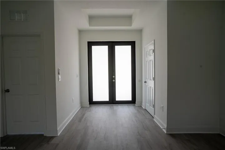 Entryway featuring black-framed double doors, wood-finish flooring, a recessed ceiling detail, and white baseboards