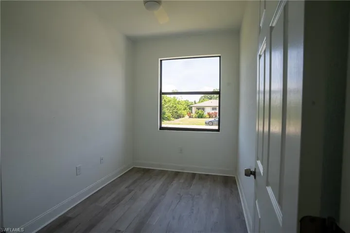 Room featuring wood-finish flooring, a contemporary window with dark framing, white trim, a ceiling fan, and a paneled interior door with a bronze-finish knob