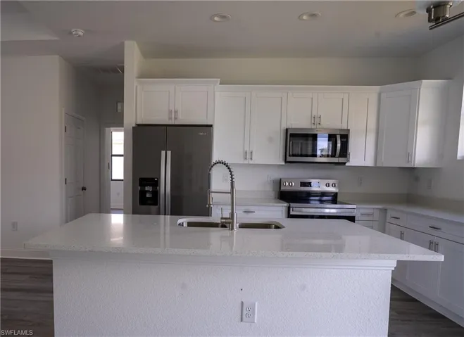 Modern kitchen featuring white shaker cabinetry, stainless steel appliances, a large center island with an integrated sink, light-toned countertops, and wood-finish flooring