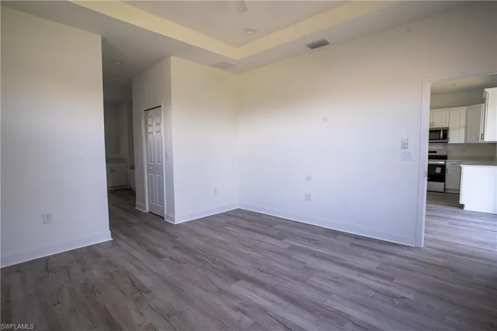 Spacious room featuring wood-finish flooring, white baseboards, and a tray ceiling