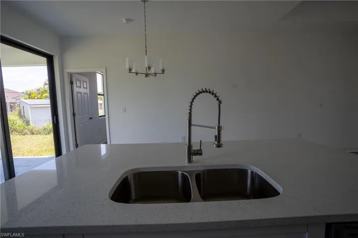 Kitchen island featuring a dual-basin stainless steel sink with a pull-down faucet, light-toned countertop, and recessed lighting