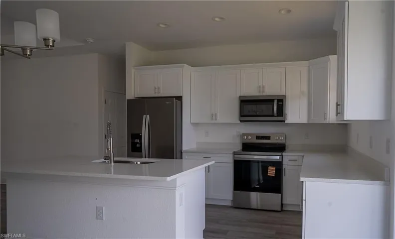 Bright kitchen featuring white cabinetry, light-toned countertops, stainless steel appliances, a kitchen island with an undermount sink, and wood-finish flooring