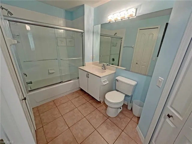 Bathroom with tile patterned flooring, enclosed tub / shower combo, vanity, and toilet