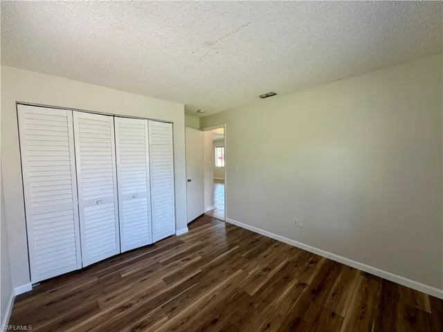 Unfurnished bedroom featuring a textured ceiling, dark wood finished floors, and a closet