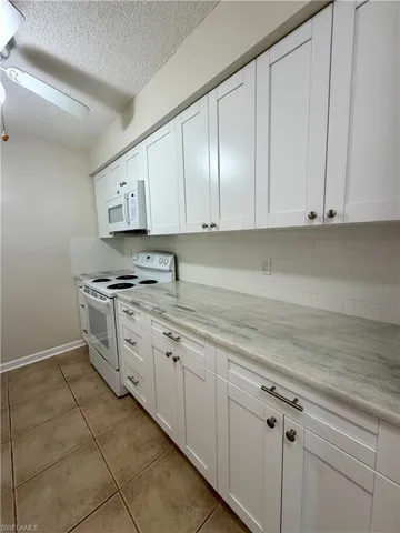 Kitchen featuring white appliances, white cabinetry, a textured ceiling, light tile patterned floors, and a ceiling fan