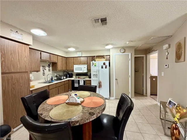 19209 - Kitchen with light countertops, white appliances, a textured ceiling, light tile patterned floors, and wood finish cabinetry