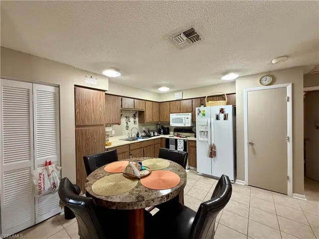 19209 - Kitchen featuring white appliances, light countertops, light tile patterned floors, a textured ceiling, and wood finish cabinetry