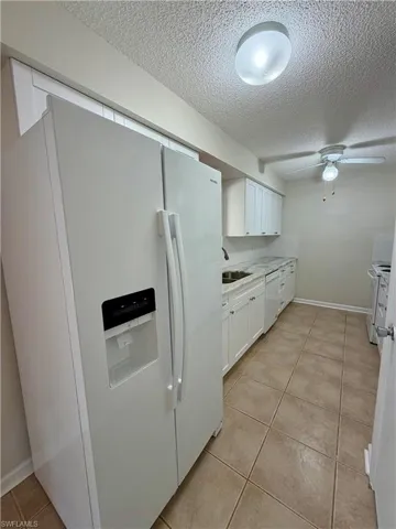 Kitchen featuring white cabinetry, white appliances, light tile patterned floors, a textured ceiling, and ceiling fan