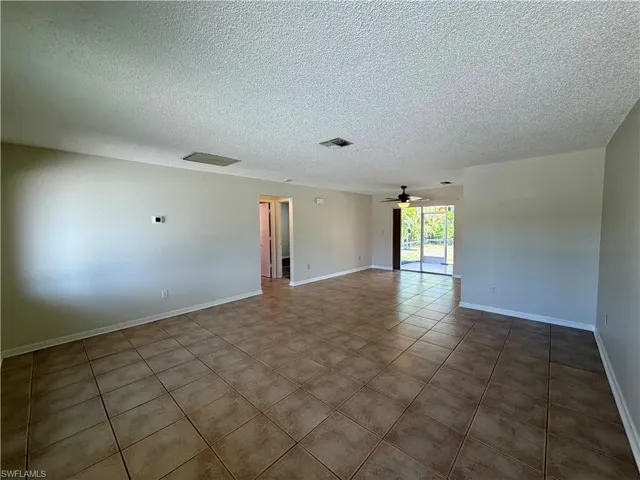 Empty room with a textured ceiling, tile patterned flooring, and ceiling fan