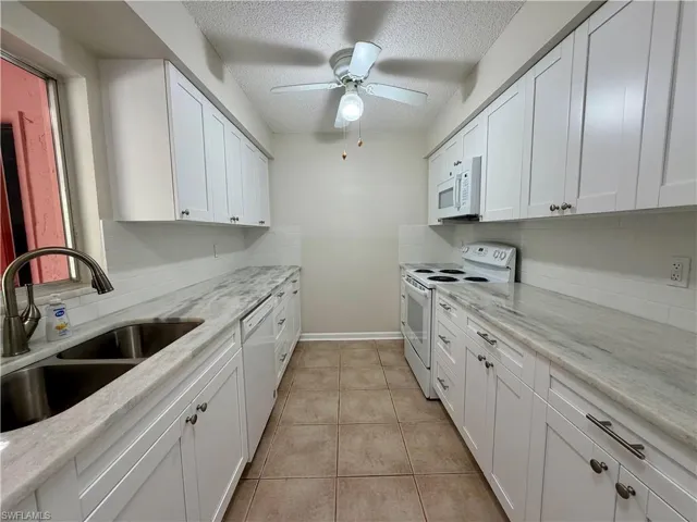 Kitchen with white appliances, white cabinetry, a textured ceiling, backsplash, and light stone countertops