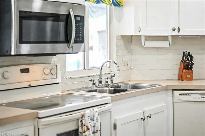 Kitchen with white appliances, white cabinetry, light countertops, and tasteful backsplash