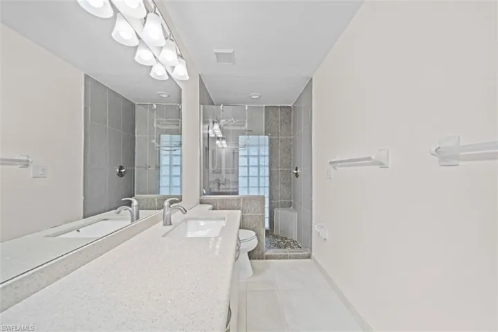 Double vanity with integrated sinks, extensive countertop space, large mirror, tile flooring, and a walk-in shower with glass block accents