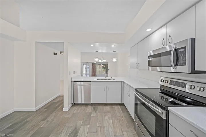 Modern kitchen featuring light cabinetry, stainless steel appliances, light countertops, a tile backsplash, and wood-finish flooring